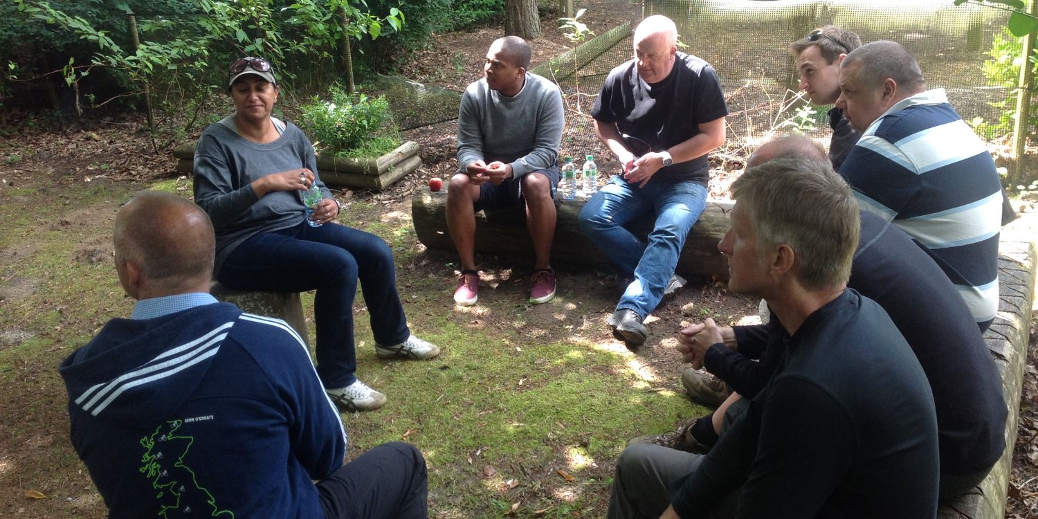Small group of colleagues in a close conversation huddle outdoors during a team walk